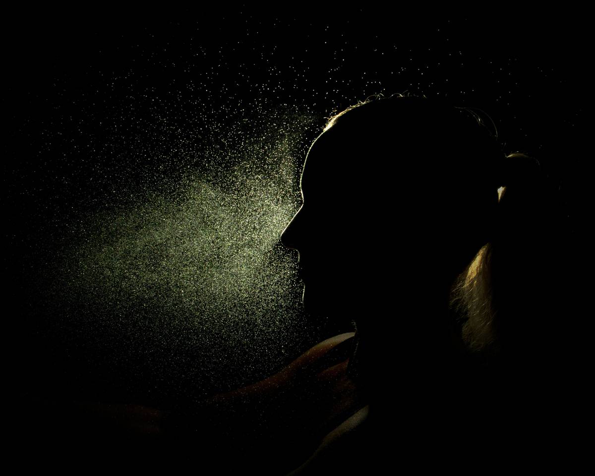 Woman using airy mist spray technique with bottle held at arm's length for even fragrance distribution